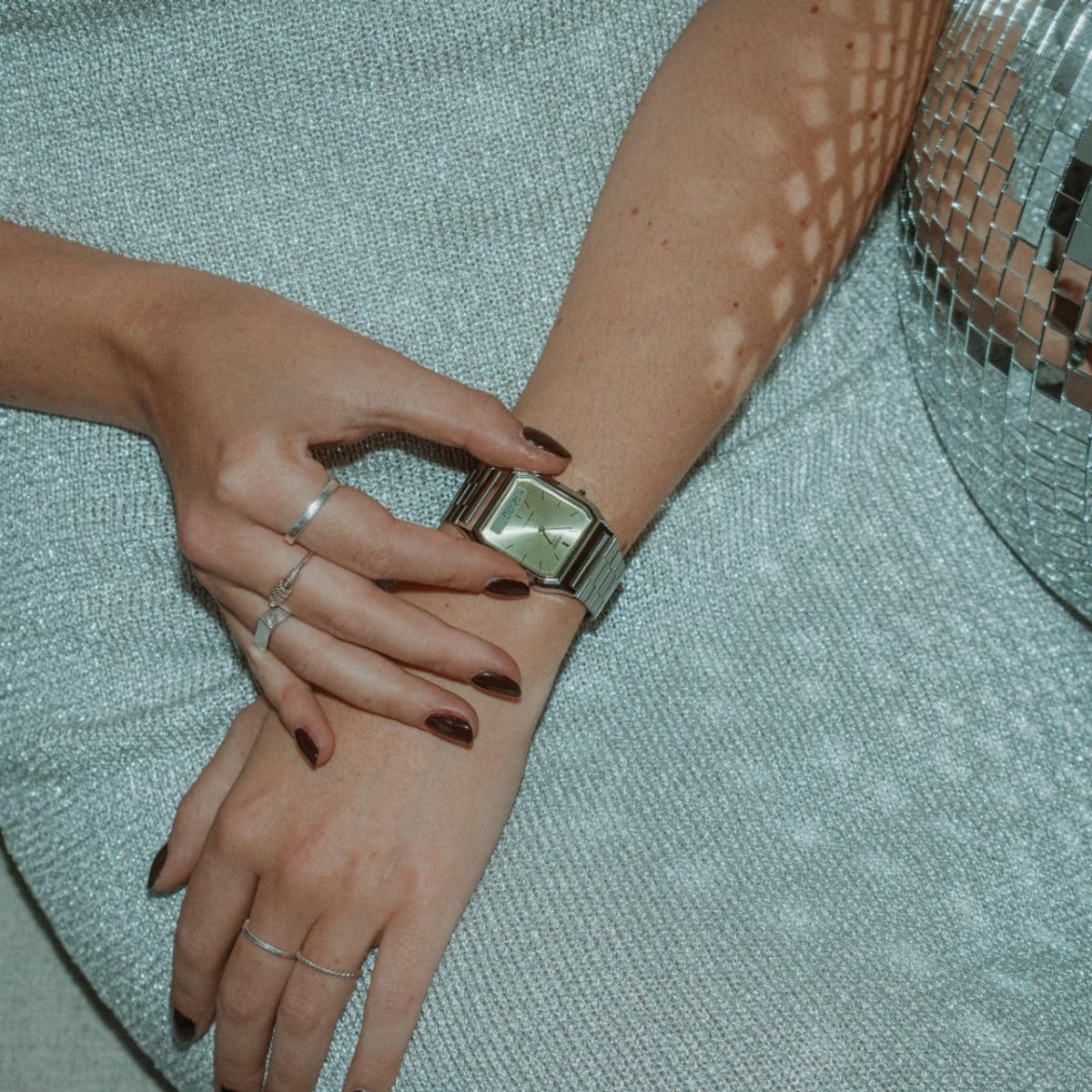 Eine Frau sitzt neben einer Discokugel und drückt auf die Knöpfe ihrer Armbanduhr, der CASIO Vintage Collection AQ-230A-9AMQYES mit hellgrüner Lünette 
