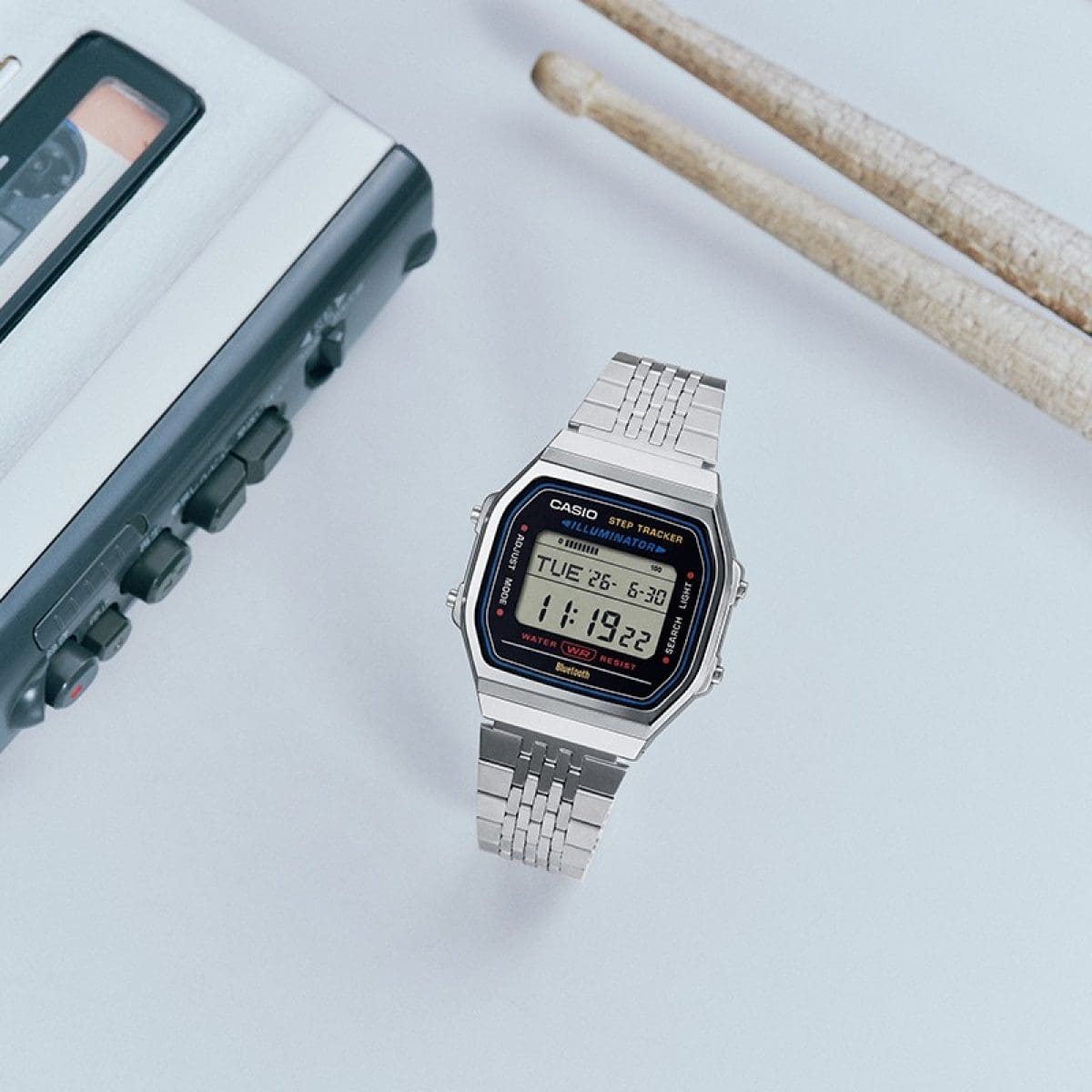 Die Uhr ABL-100WE-1A mit Schlagzeugstöcken und Audiogeräten platziert.