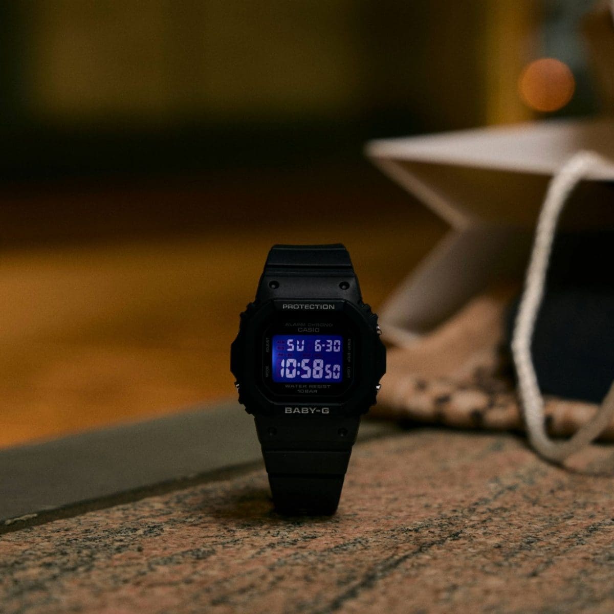 Die BGD-565U-1ER steht auf einer steinigen Fläche vor einem warm beleuchteten Hintergrund. Das blaue Display leuchtet dabei. 