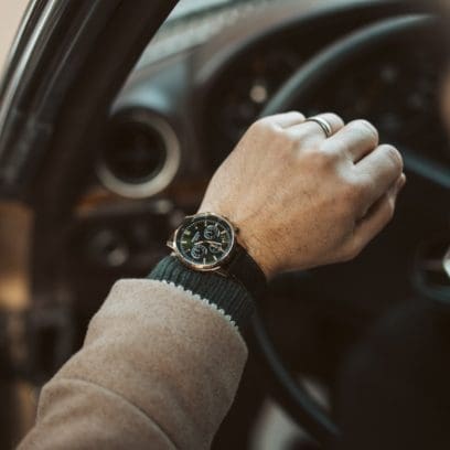 Nahaufnahme der grünen EDIFICE-Uhr EFR-575CL-3AEF am Handgelenk eines Mannes in einem Auto, der das Lenkrad festhält.