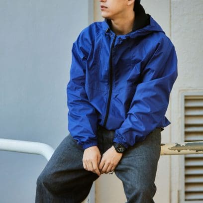 Ein Mann mit blauer Jacke und Jeans sitzt auf einem Metallgeländer, am Handgelenk sieht man die G-SHOCK GA-2100-1A Armbanduhr