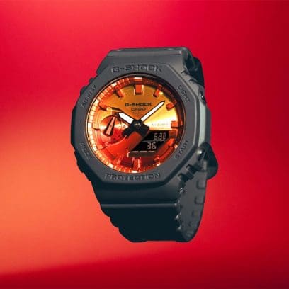 G-SHOCK GA-2100FL-8A mit orangenem Zifferblatt und grauem Armband vor einem roten Hintergrund