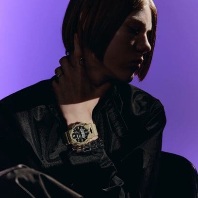 Die beleuchtete G-SHOCK Armbanduhr GA-010-5A am Handgelenk einer abgedunkelten Person vor violettem Hintergrund.