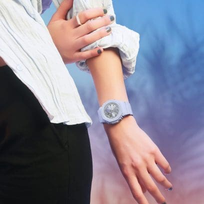 Halbtotale einer Frau, die eine weiße Bluse hochgekrempelt und am Handgelenk die fliederfarbene GMA-P2100SG-2AER Armbanduhr von G-SHOCK trägt