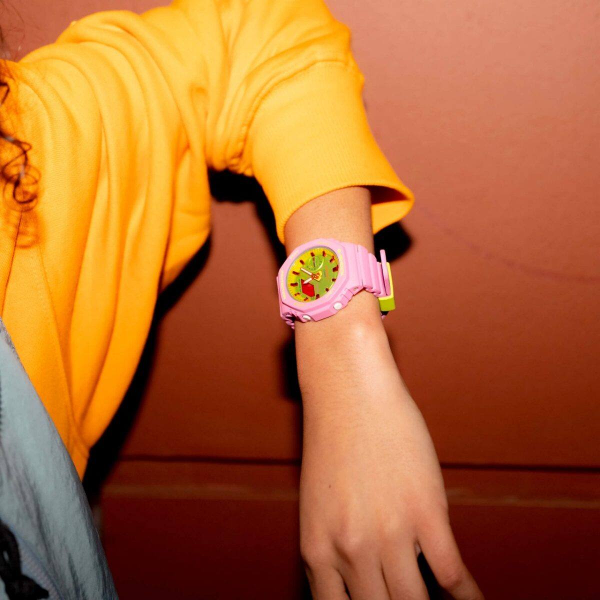 Eine Frau trägt eine G-SHOCK Uhr aus der "Bright Summer" Kollektion mit pinkem Armband und ist dabei eine Süßigkeit