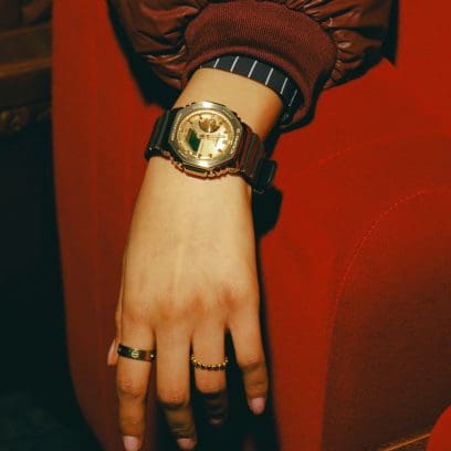 Nahaufnahme der GM-2100YMG-9A9ER am Handgelenk einer jungen Frau. Der Arm ruht dabei auf einem roten Kinosessel. An zwei Fingern trägt sie Goldringe. 