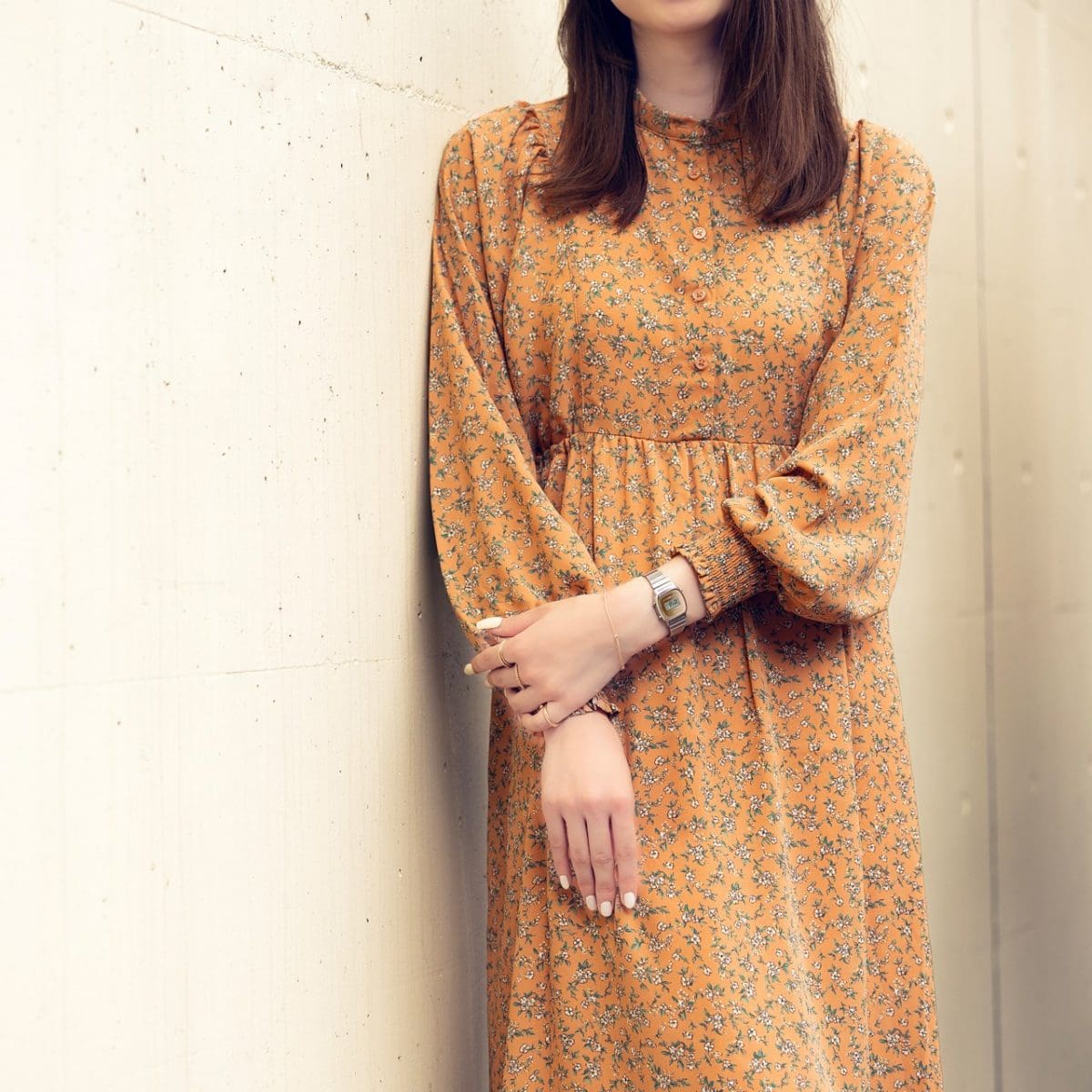 Eine Frau mit langen braunen Haaren trägt ein orange-blau gemustertes langes Kleid und am Handgelenk die Digitaluhr LA670WES-4A mit kleinem quadratischem Gehäuse.