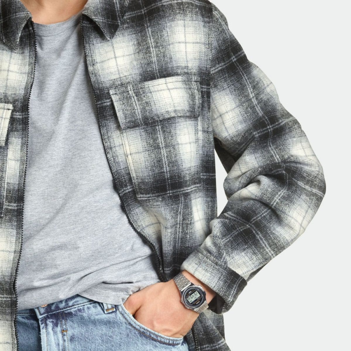 El hombre viste una camisa de cuadros blancos y negros y una camiseta gris. En su muñeca lleva un reloj redondo plateado A171WE-1A con pulsera de acero inoxidable.