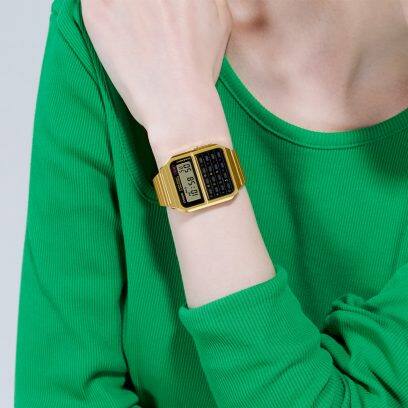 El reloj de pulsera dorado CASIO CA-500WEG-1A en la muñeca de una mujer con camisa verde