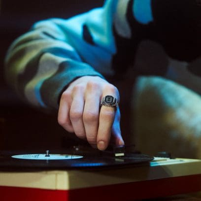 Primer plano de una mano moviendo la aguja de un tocadiscos. La persona lleva el CASIO Ringwatch CRW-001 con pantalla digital en el dedo índice.