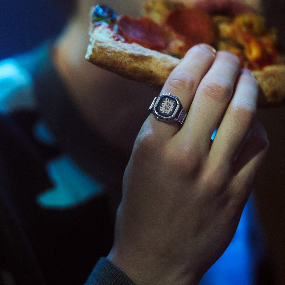 Primer plano de una mano sosteniendo una pizza. El CASIO CRW-001 Ringwatch está en el dedo índice.