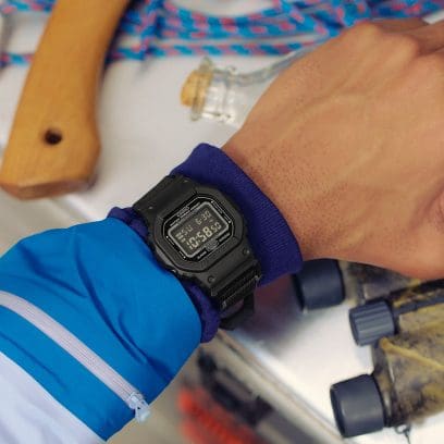 Un hombre que viste una chaqueta azul lleva puesto en la muñeca un reloj de pulsera negro DW-5600MNC-1ER.