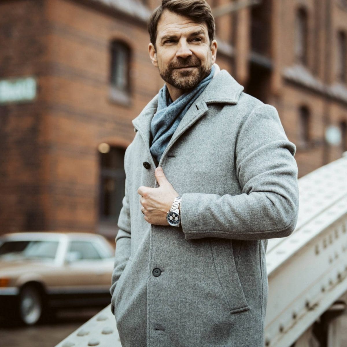 El reloj cronógrafo EFR-575D-2AEF con correa metálica en la muñeca de un hombre que está de pie frente a un edificio de ladrillos.