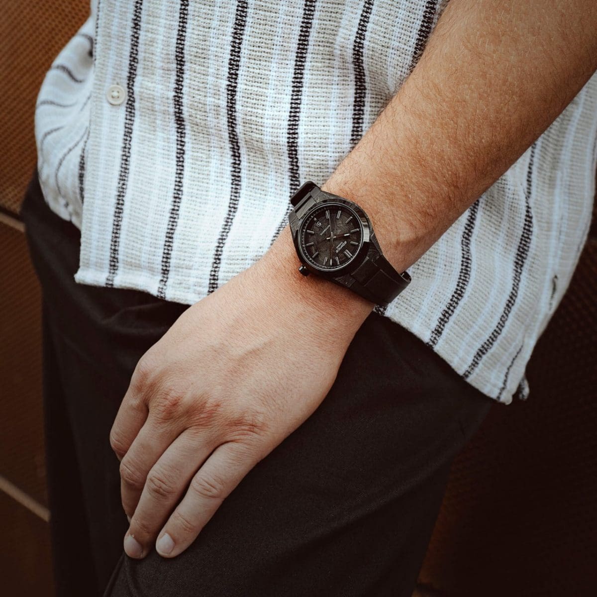 El EFK-100XPB-1AER en la muñeca de un hombre que viste una camisa a rayas blancas, negras y beige.