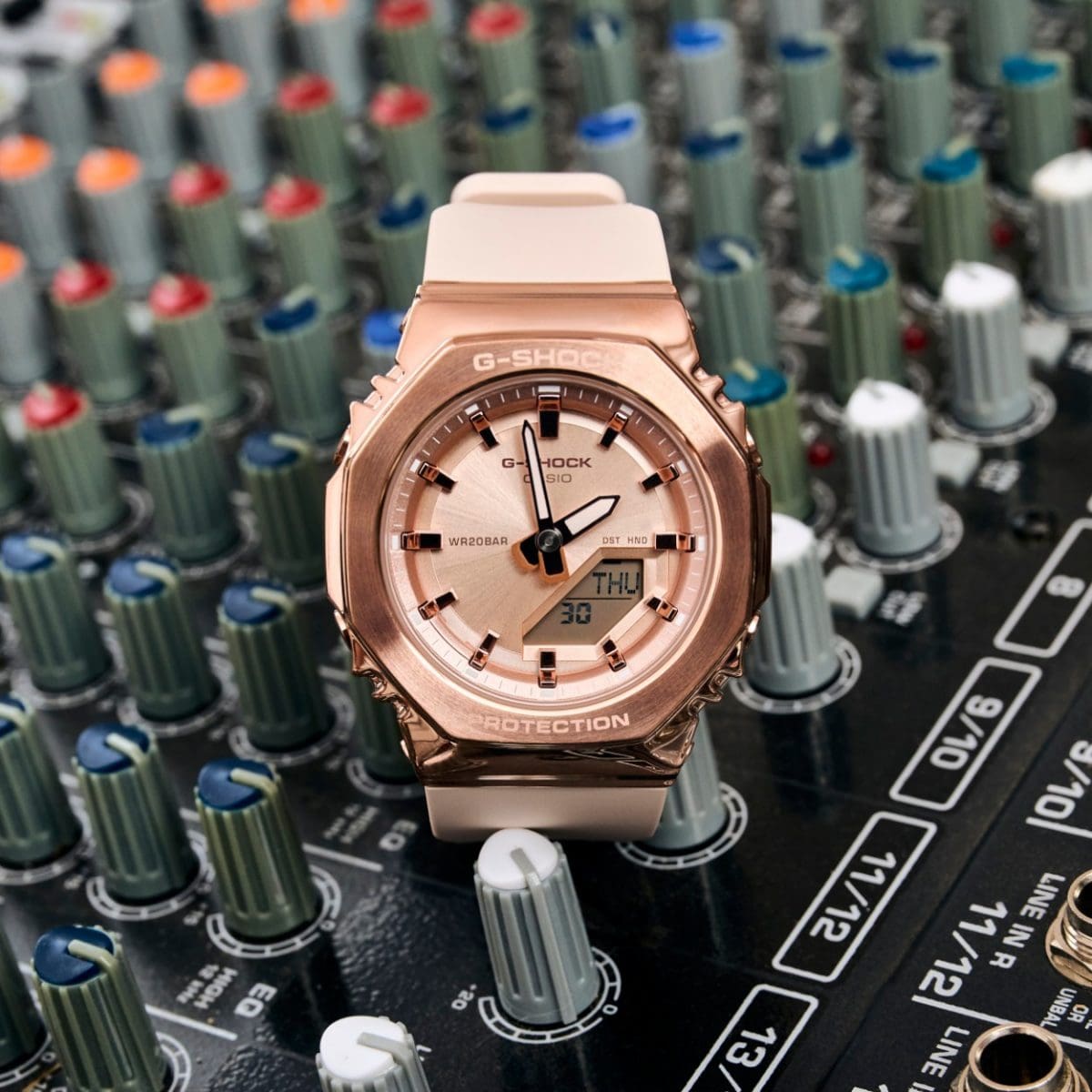 El reloj de pulsera GMA-S2110PG-4A con caja de metal en oro rosa y correa de resina beige sobre una mesa de mezclas