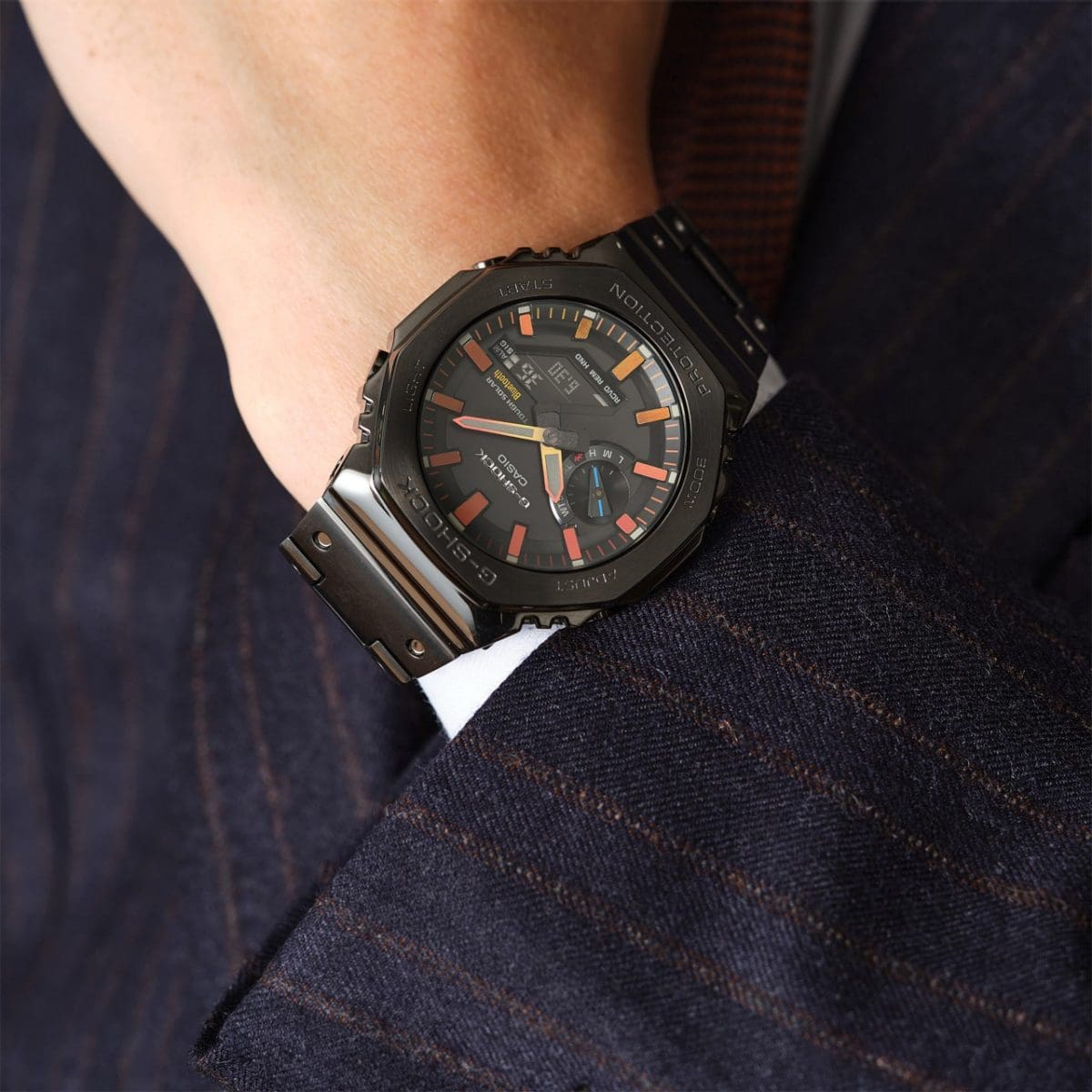 El reloj de pulsera CASIO GM-B2100BPC-1A de acero inoxidable en la muñeca de una persona vestida de traje