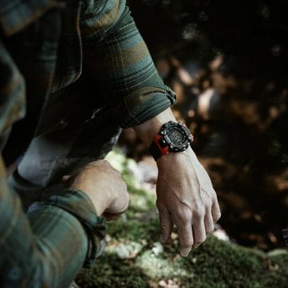 El reloj de pulsera GW-9500-1A4 en la muñeca de un hombre con camisa verde a cuadros. Al fondo se ve el suelo del bosque