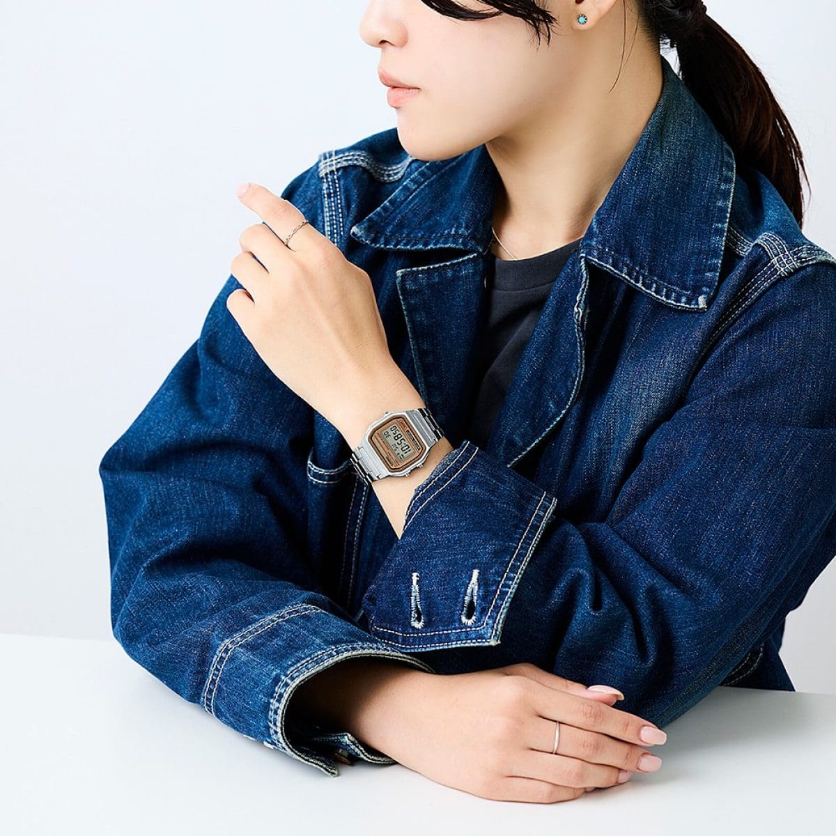 Woman in denim jacket with rings wears A158WEA-9 digital watch on her wrist and relaxes against a white table