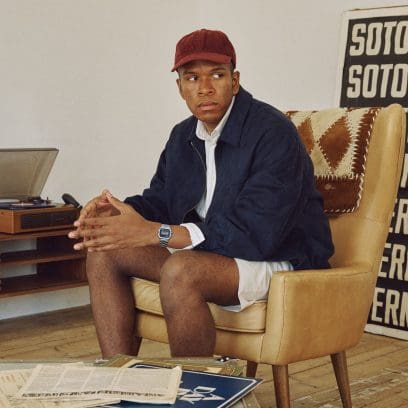 A man wearing a dark blue jacket and a red baseball cap sits in an armchair and wears the A158WEA-2EF on his wrist.