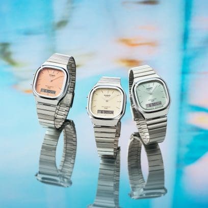Three watch models from the AQ-240E series in orange, cream and light blue stand side by side on a blue, mirrored background.