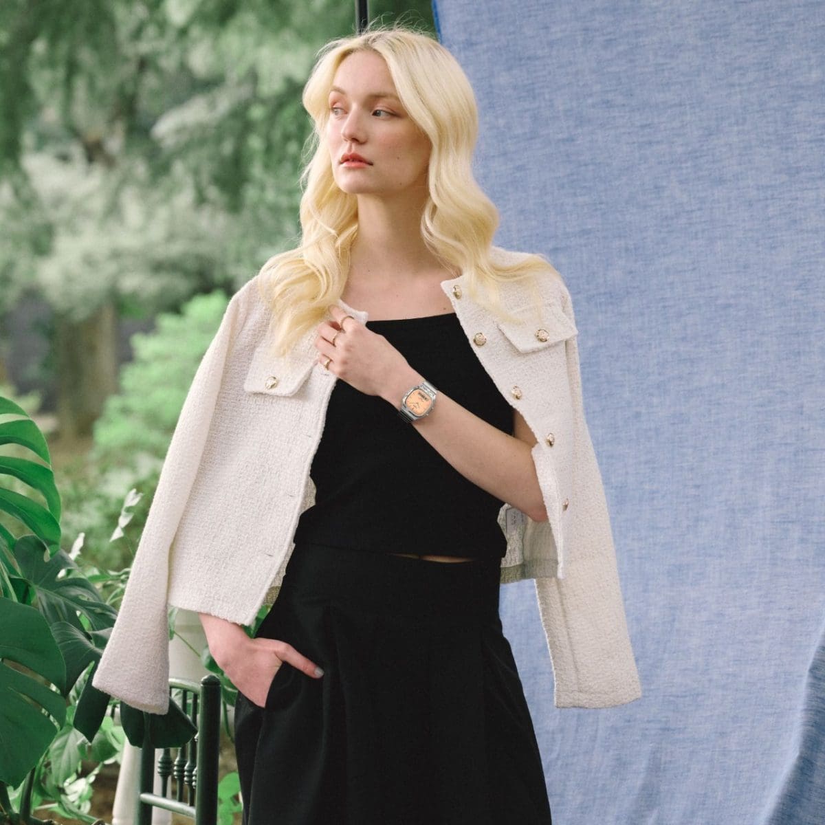 A woman in a black outfit with a cream-colored jacket draped over her shoulders wears the silver AQ-240E-4AEF with an orange dial on her wrist.