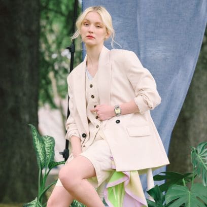 A blonde woman in a beige outfit sits on a stool and wears the CASIO AQ-240E-7A2EF analog-digital wristwatch on her wrist.
