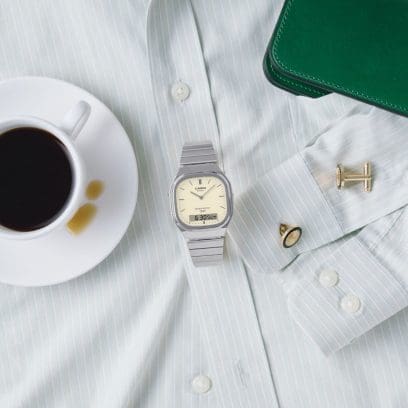 The silver wristwatch AQ-240E-7A2EF lies on a light grey shirt, on which gold cufflinks also lie.