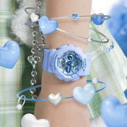 The BA-110YK-2A BABY-G wristwatch on a woman's wrist, surrounded by illustrations of blue hearts.