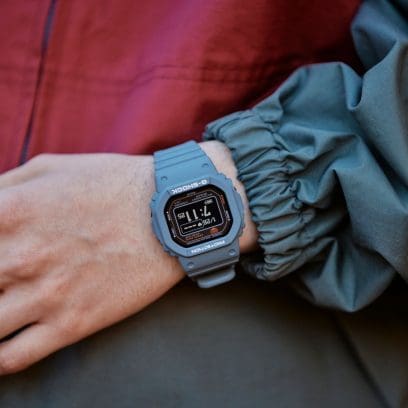 The dove-blue DW-H5600-2 wristwatch on the wrist of a person wearing a light anorak