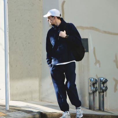 A man in a dark track suit and a white cap is standing at the corner of a building