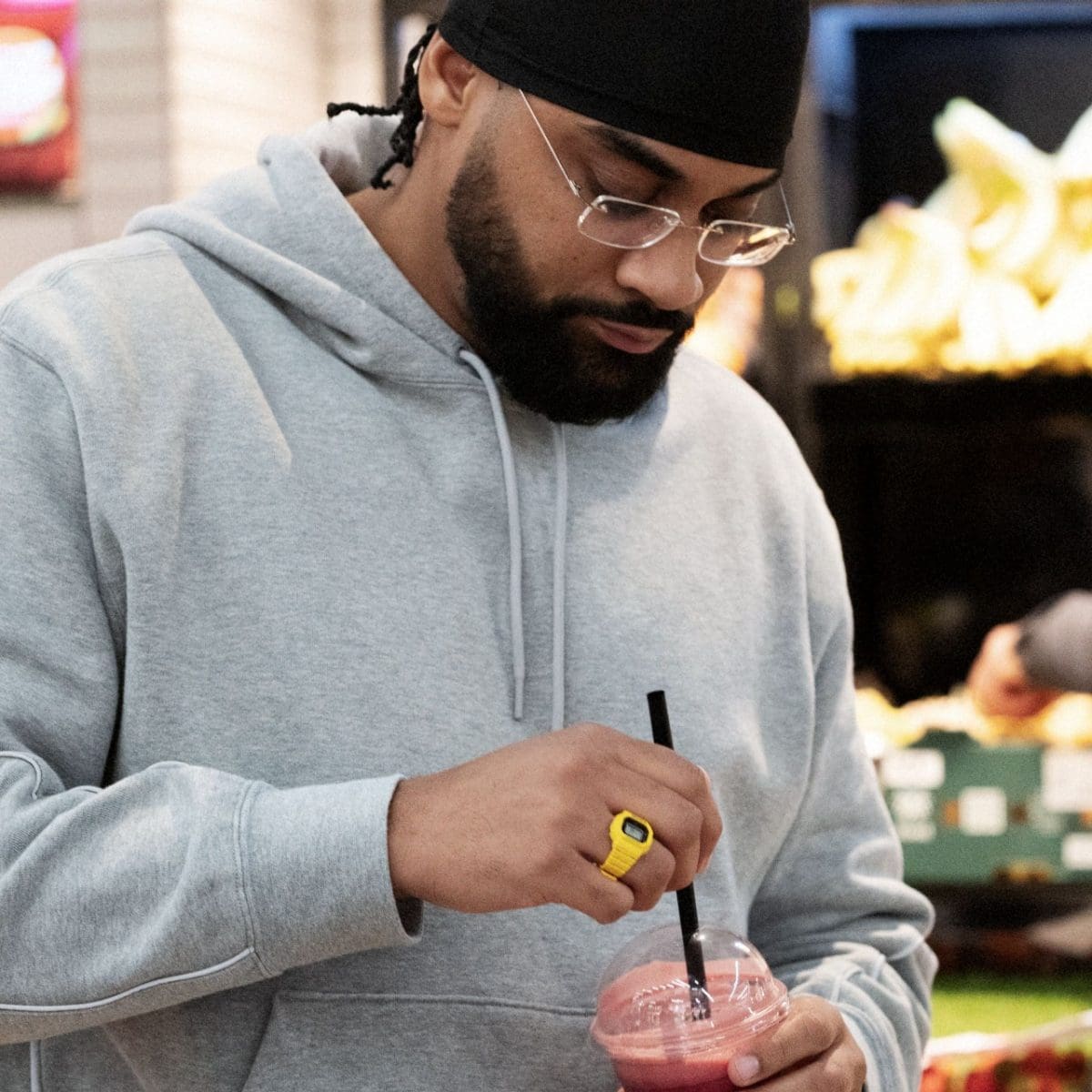 A man wearing a grey sweater is wearing the DWN-5600-9ER on his ring finger and stirring a drink with a straw