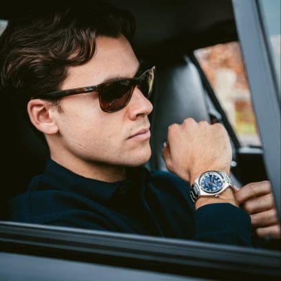 A man wearing a black top and sunglasses is sitting in a car and wearing the EFB-109D-2AVEF