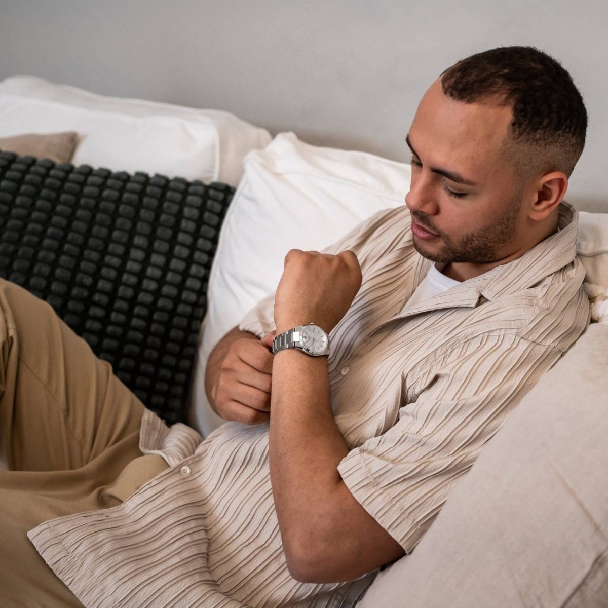 A man wearing a beige shirt sits on a sofa and wears the EDIFICE EFK-110D-7A on his wrist