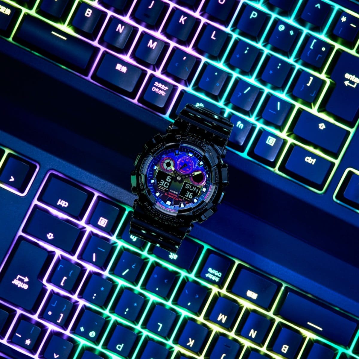 The G-SHOCK GA-100RGB-1A with colourful bezel and black strap on a colourful gamer keyboard