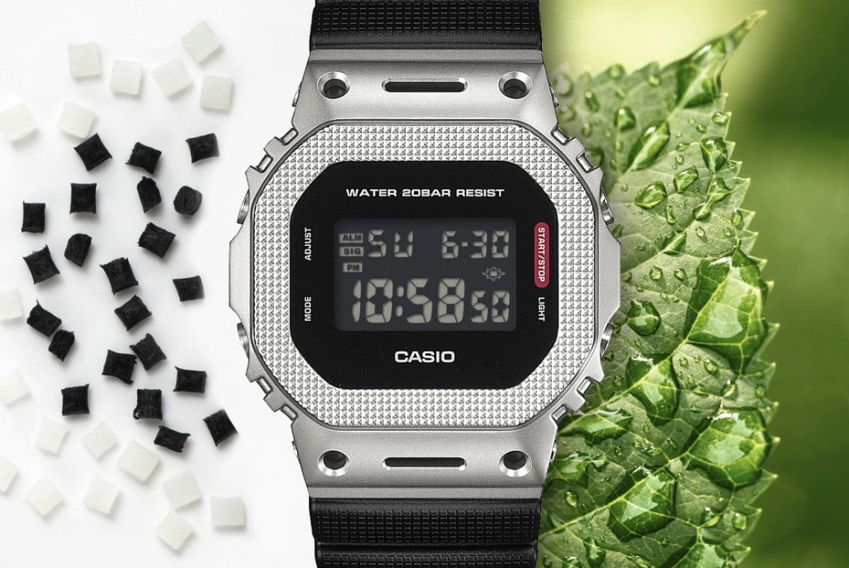 The GM-5600M-1ER is shown next to a green leaf with water droplets on it. On the other side, white and black spheres of the bio-based resin are visible.