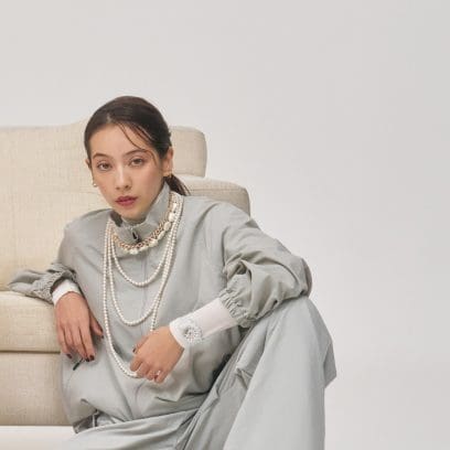 A woman wearing a white sweater and gray jacket leans on a sofa and wears the beige white GMA-P2100M-7A on her wrist