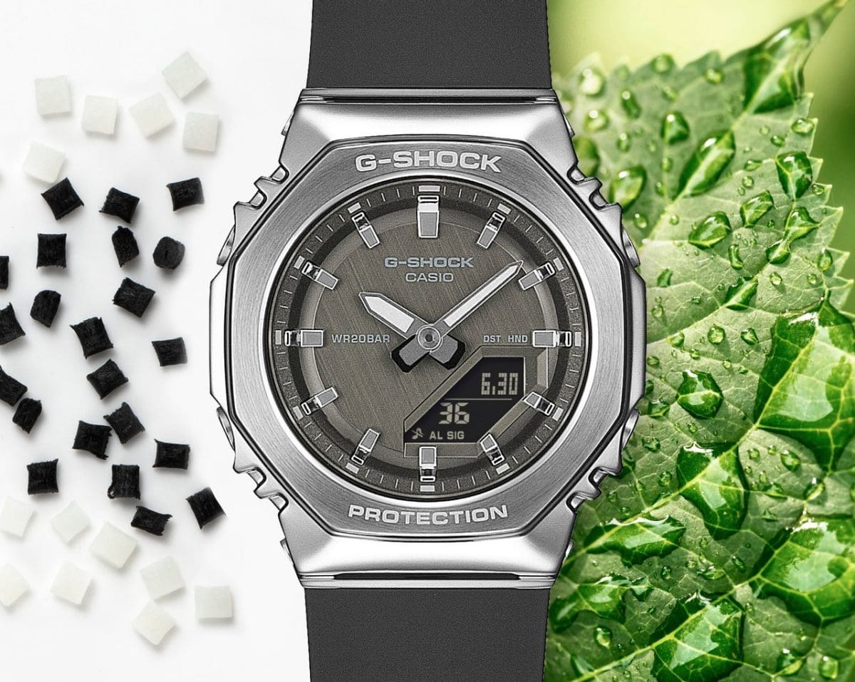 The GM-S2110-1A1ER in the center is framed by a green leaf with water droplets on the right and white and black spheres of the bio-based resin on the left.