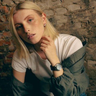 A young woman wears the GM-S2110-2AER on her left wrist. She also wears a white T-shirt paired with a green jacket. 