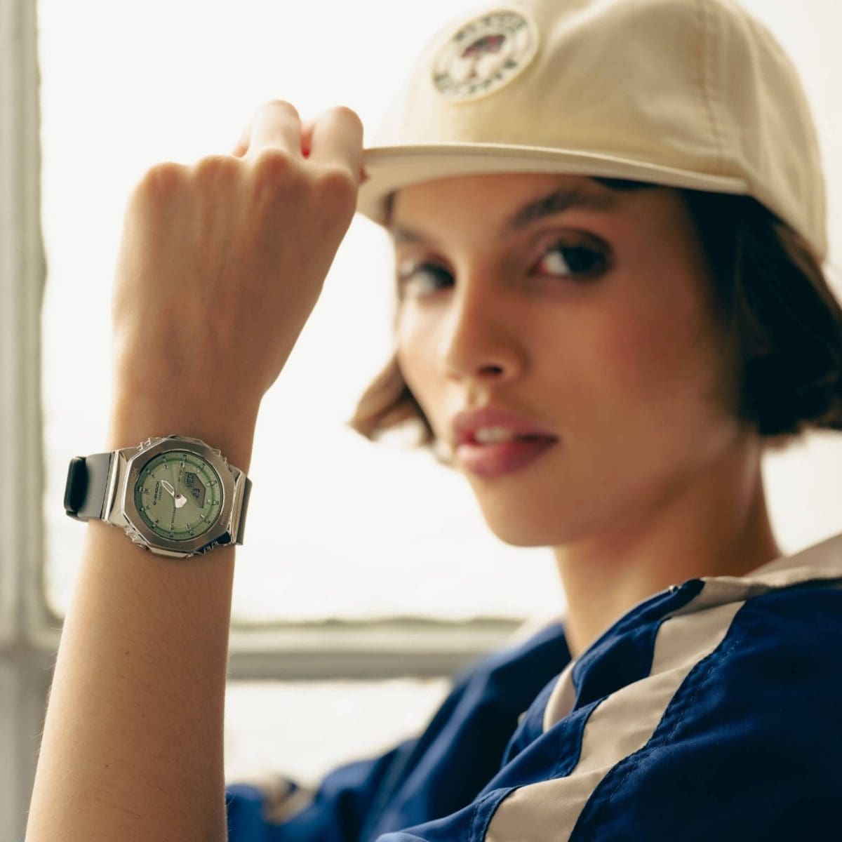 A young woman wearing a beige cap and a sporty blue jacket shows off the GM-S2110-3A on her left wrist. 