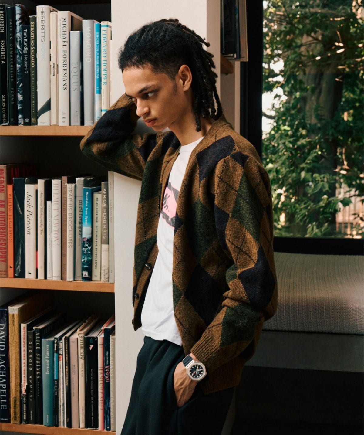 A man wearing a plaid cardigan leans against a bookshelf and wears the GM-2100M-1AER on his wrist.