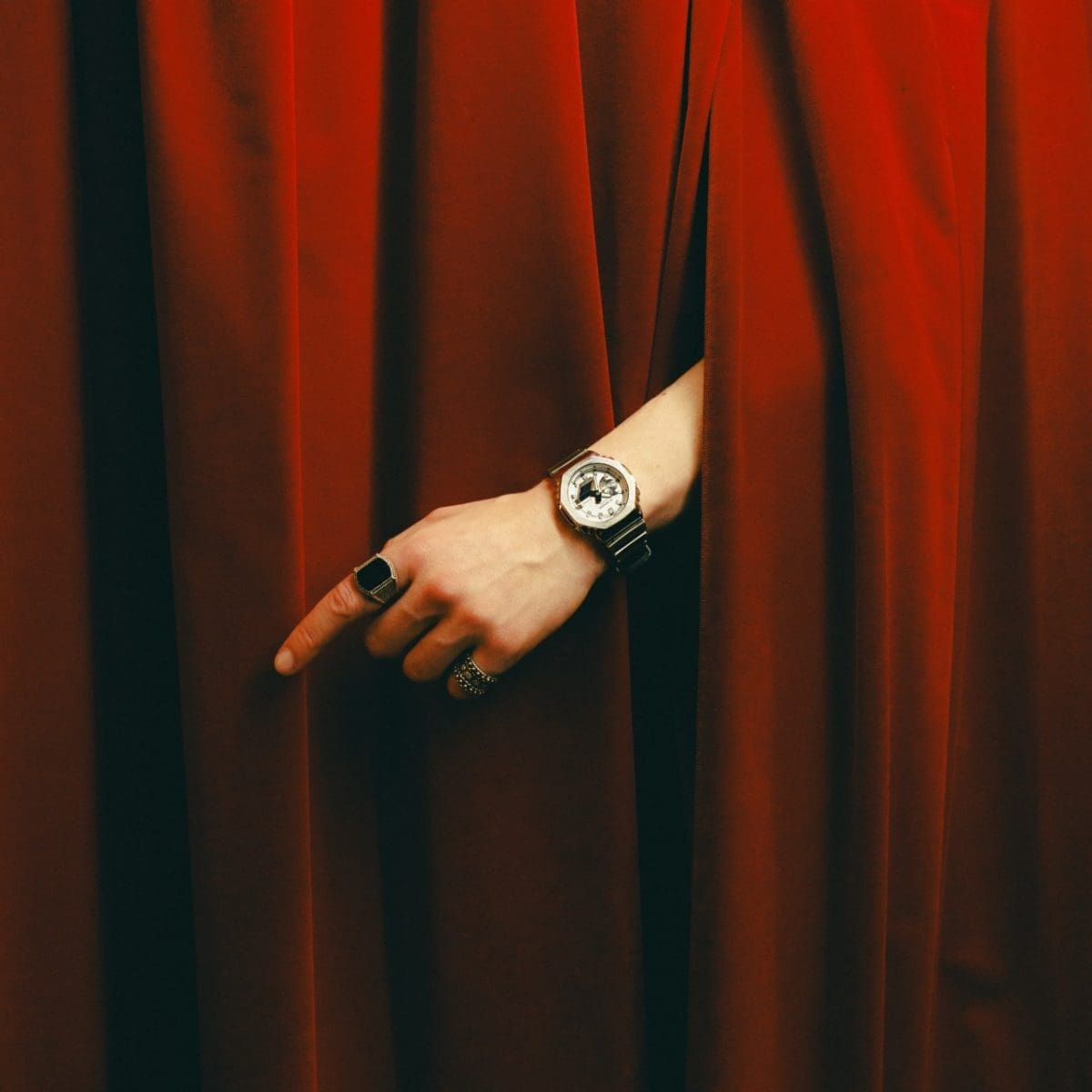 Close-up of the GM-2100YM-8ER on the left wrist of a model in front of a red curtain.
