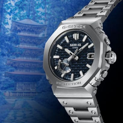 A side view of the silver MRG-B2100D-2ADR with a blue dial. A mountain pagoda can be seen in the background.