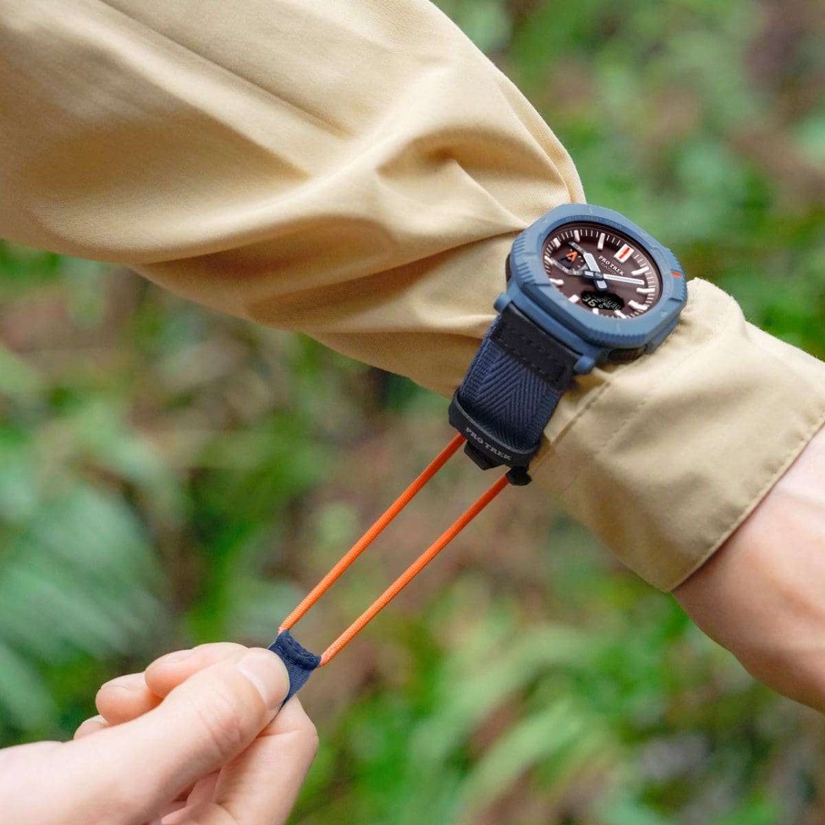 Close up on a man's wrist wearing a beige jacket and the PRO TREK PRJ-B001B-2 and pulling on the orange strap