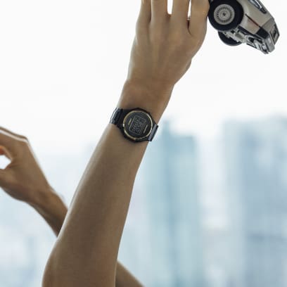 A person holds up a toy car and wears the Casio wristwatch ‘TRN-50ZE-1A’ in black with gold-coloured details on his wrist