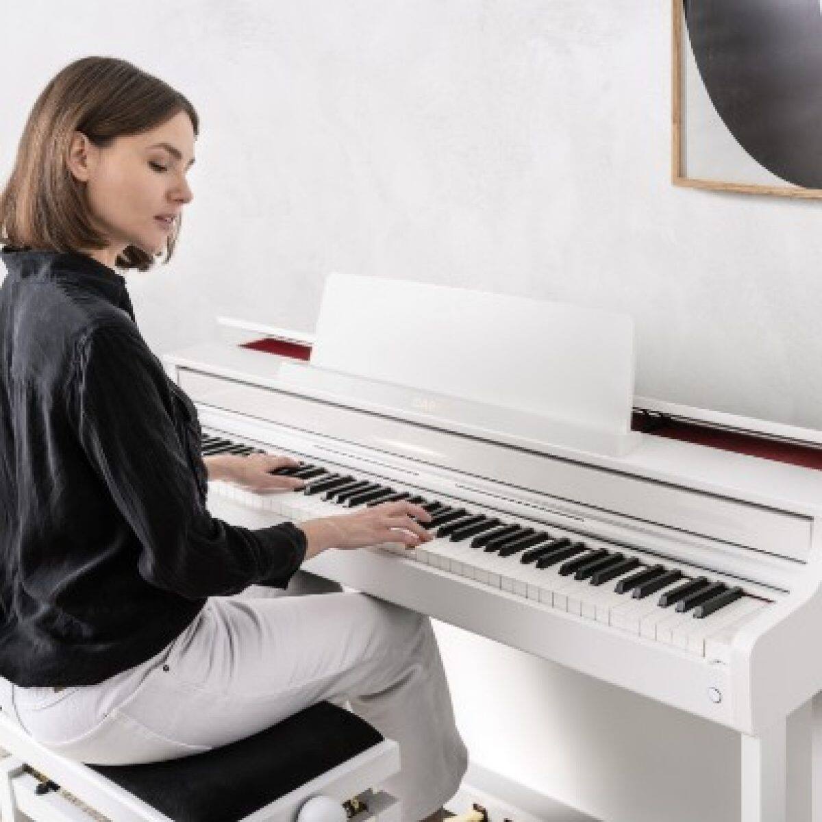 Une femme est assise devant le piano numérique blanc CELVIANO AP-550 dans le salon.