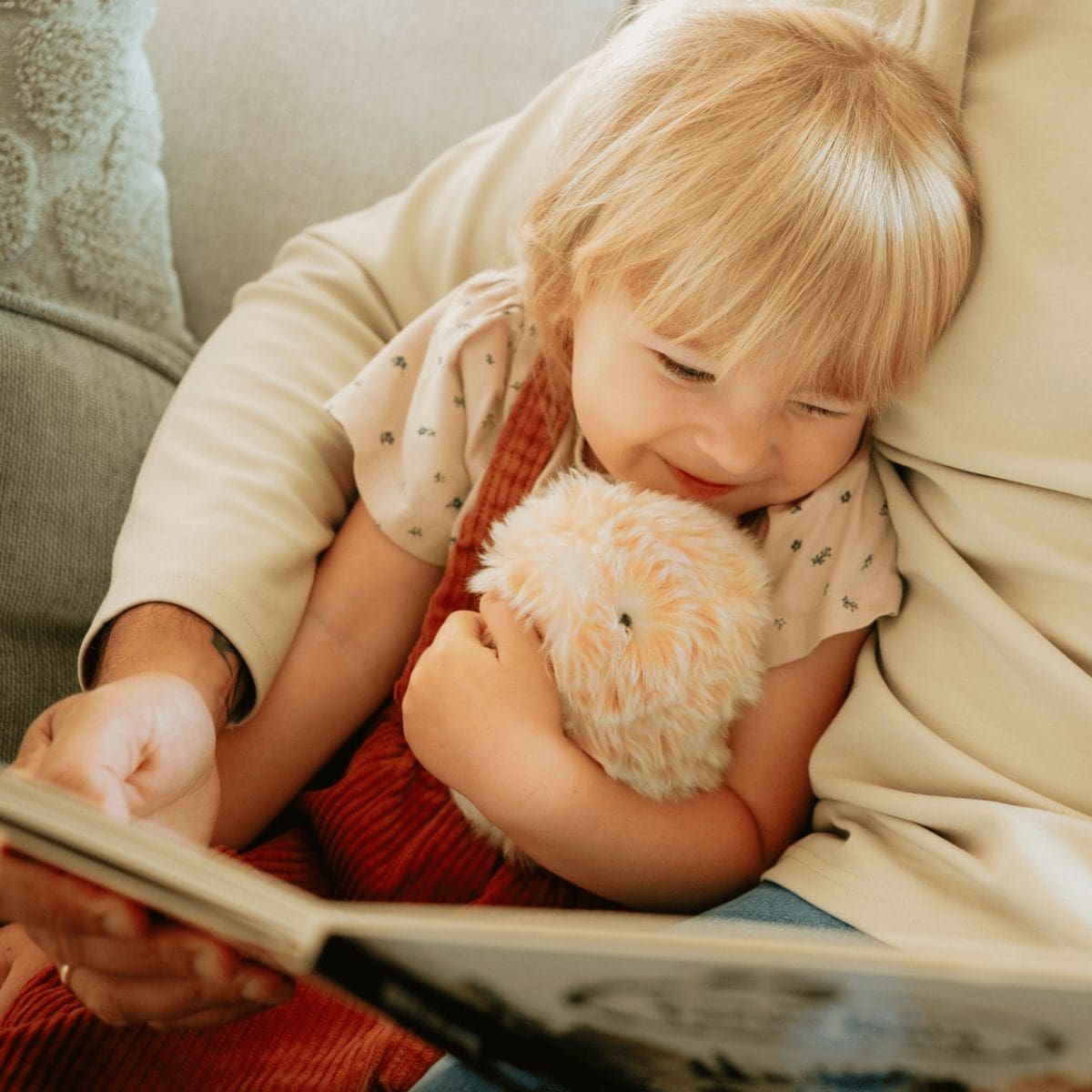 Un enfant est allongé dans les bras d'un adulte, à qui l'on lit un livre, et qui tient le Moflin doré dans ses bras.
