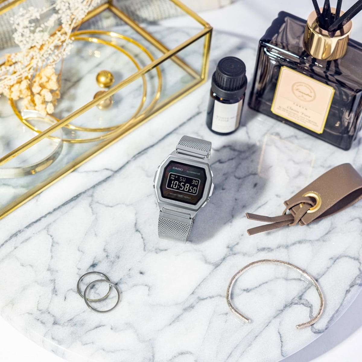 Montre numérique A1000M-1B avec bracelet en maille d'acier inoxydable sur dessus en marbre entouré de bijoux, parfum d'ambiance et accessoires