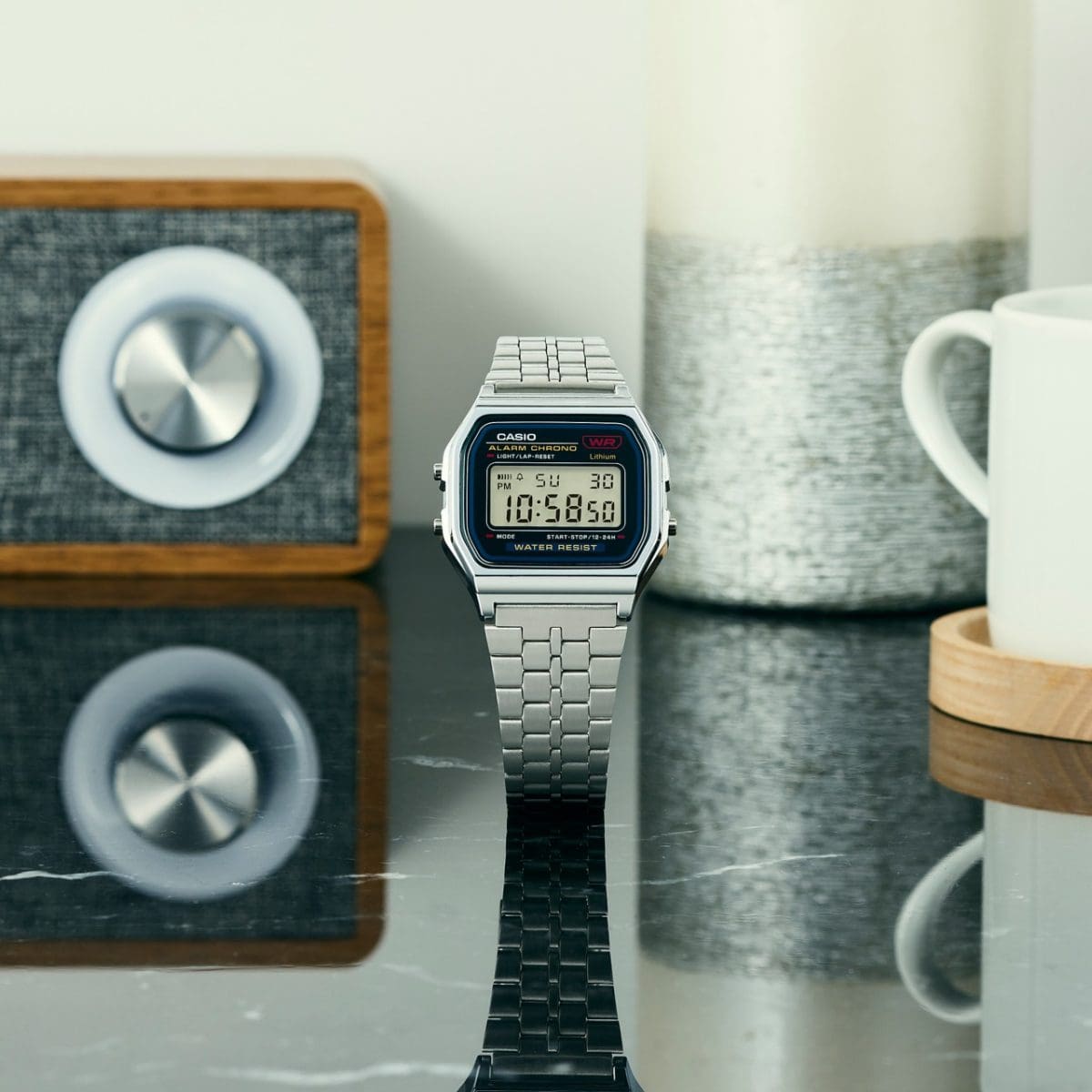 La montre-bracelet numérique A159WE-1EF est posée sur une table aux reflets brillants, avec une radio moderne et une tasse en arrière-plan