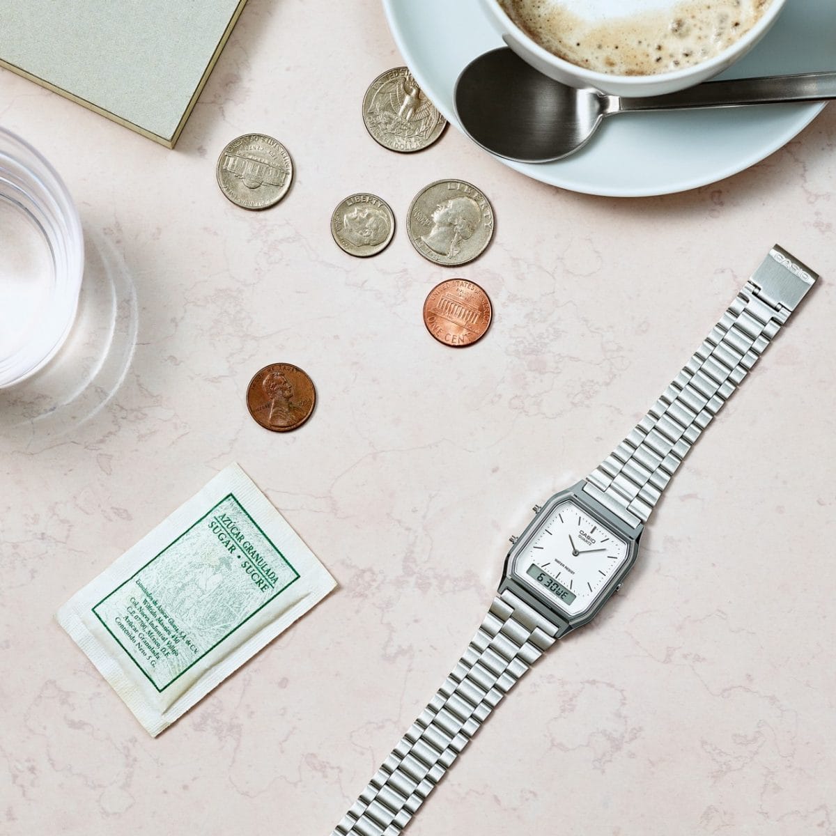 L'AQ-230A-7DMQ posé à plat sur une table avec des pièces de monnaie et une tasse de café à côté
