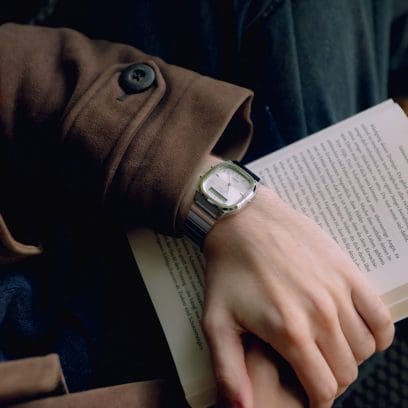 Un homme vêtu d'une veste en laine marron porte l'AQ-240E-7AEF au poignet. Sa main repose sur un livre ouvert.